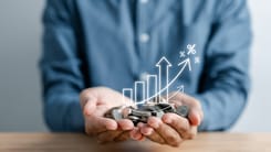 Haende mit Muenzstapel und wachsender Zinsgrafik als Symbol fuer Rendite oder Kapitalwachstum.