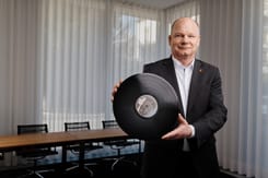 mann im anzug praesentiert eine grosse vinyl-schallplatte in einem modernen buero oder meetingraum