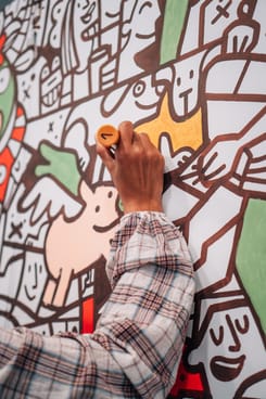Hand einer Teilnehmerin beim Ausmalen der Illustrationswand am GLKB-Stand mit orangefarbenem Stift.