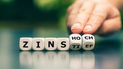 Hand dreht Buchstabenwuerfel mit dem Wort ZINS und Auswahl zwischen HOCH und TIEF.