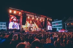 Openair-Konzert beim Sound of Glarus mit beleuchteter Bühne, Musikern und grossem Publikum bei Nacht.