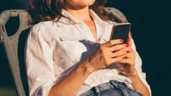 Frau in weisser Bluse entspannt im Freien und nutzt ihr Smartphone bei sonnigem Wetter.