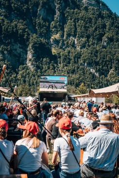 Besuchende verfolgen ein Schwingfest auf Grossbildschirm in alpiner Umgebung mit geselliger Festatmosphäre