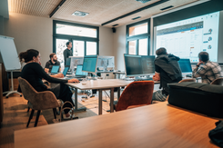 Team arbeitet gemeinsam an digitalen Projekten während eines Workshops mit Präsentation und moderner IT-Infrastruktur.