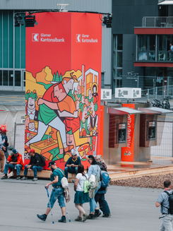 Bankomaten mit bunter Illustration und wartenden Personen am ESAF 2025 Gelände.