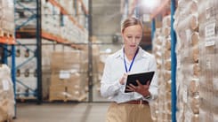 Frau mit Tablet kontrolliert Warenbestand in einem grossen Hochregallager.