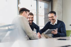 Persönliche Beratung im Büro: Drei Männer sitzen zusammen und besprechen Inhalte auf einem Tablet.