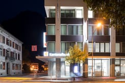 Nachtaufnahme des GLKB-Hauptsitzes in Glarus mit beleuchteter Fassade und moderner Architektur.