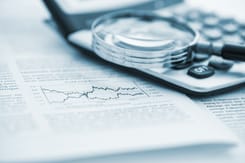 Nahaufnahme von Lupe und Taschenrechner auf einem Finanzbericht mit Börsendiagramm und Text.