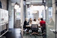 Mehrere Personen im Austausch während eines Meetings in einem modernen Besprechungsraum mit Glaswänden.