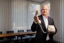 mann im anzug praesentiert ein klassisches analoges festnetztelefon mit hoerer in einem modernen buero