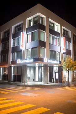 Nachtaufnahme des GLKB-Hauptsitzes in Glarus mit beleuchteter Fassade und moderner Architektur.