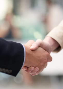 Zwei Personen geben sich die Hand bei einem Geschäftstreffen als Zeichen für Partnerschaft und Vertrauen.