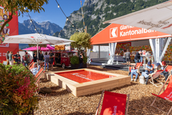 Gemütliche Begegnungszone am Promostand der GLKB mit Liegestühlen, Infostand und Dekoration vor Bergkulisse.