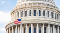 Detailansicht der Kuppel des US-Kapitols mit wehender amerikanischer Flagge im Vordergrund.