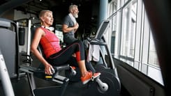 Aelteres Paar trainiert gemeinsam auf Fitnessgeraeten in einem modernen Fitnessstudio.