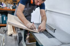 Handwerker misst präzise eine Holzplatte in einer Werkstatt – Symbolbild für regionales Handwerk und KMU.