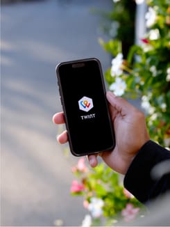 Person hält Smartphone mit gestarteter TWINT App im Freien, umgeben von Blumen und Tageslicht.