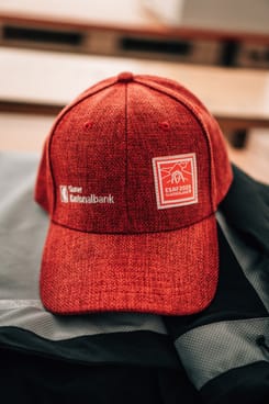 Rote GLKB-Basecap mit ESAF-Logo liegt auf einer Jacke – offizielles Accessoire am ESAF 2025.