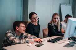 Mitarbeitende arbeiten gemeinsam an einem Computer und besprechen digitale Inhalte in konzentrierter Arbeitsatmosphäre.