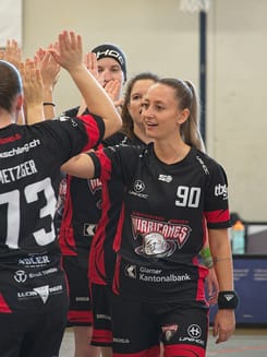 Unihockey-Spielerinnen feiern mit High-Five auf dem Spielfeld während eines Teammoments in der Halle