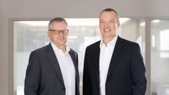 VRP Urs Gnos und CEO Sven Wiederkehr in Businesskleidung stehen gemeinsam in modernen Büroräumen der Glarner Kantonalbank und blicken in die Kamera.