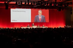 Generalversammlung der GLKB mit Redner am Podium vor grossem Publikum in festlich beleuchtetem Saal.