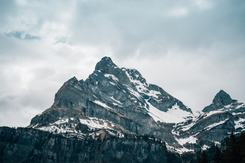 Schneebedeckter Berggipfel in den Schweizer Alpen unter bewölktem Himmel als eindrucksvolle Landschaftsaufnahme.
