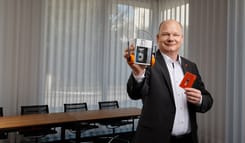 mann im anzug praesentiert einen retro kassettenplayer mit kopfhoerern und eine audio kassette in einem modernen buero