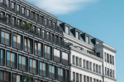 Moderne und klassische Wohngebäude mit grossen Fenstern und Balkonen vor blauem Himmel in urbaner Umgebung.