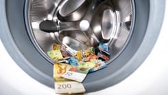 Schweizer Banknoten liegen in der Trommel einer Waschmaschine als Symbol fuer Geldwaesche.