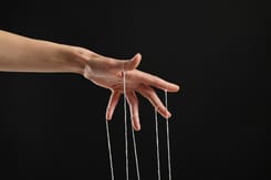 Hand mit gespannten Fäden symbolisiert Kontrolle, Manipulation und unsichtbare Einflussnahme.