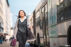 Geschäftsfrau steigt aus dem Bus in der Stadt, Symbolbild für mobiles und papierloses E-Bill-Management.