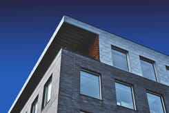 Modernes mehrstöckiges Gebäude mit dunkler Backsteinfassade und grossen Fenstern, fotografiert aus der Froschperspektive vor blauem Himmel.
