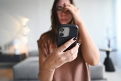 Frau mit Smartphone hält sich die Stirn, wirkt gestresst oder überfordert nach versuchtem Telefonbetrug im modernen Wohnraum.