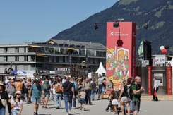 Besucher schlendern über das ESAF-Festivalgelände vor dem markanten roten GLKB-Turm mit Illustrationen.