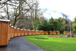 Markthäuschen des Weihnachtsmarkts in Glarus entlang eines Parkwegs mit Wiese, Bäumen und Bergkulisse im Hintergrund.