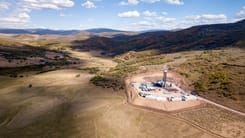 Luftaufnahme einer Bohranlage auf einem abgelegenen Feld inmitten einer huegeligen Landschaft.