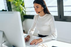 Junge Frau mit Headset arbeitet konzentriert am Computer im Kundenservice und bietet digitale Unterstützung an.