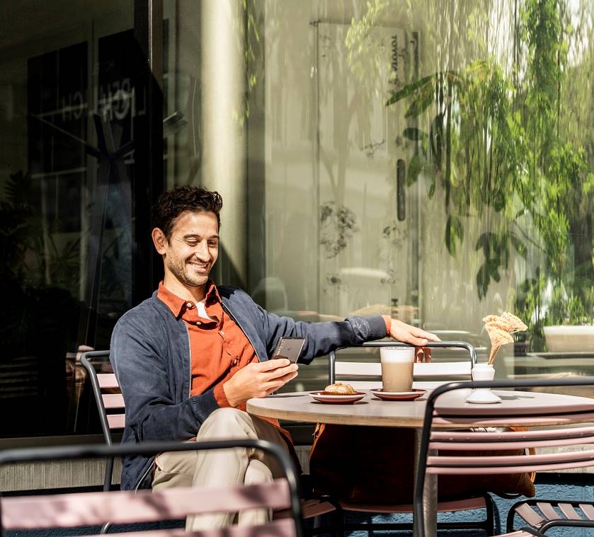 Mann mit Mobile in der Hand sitzt im Café