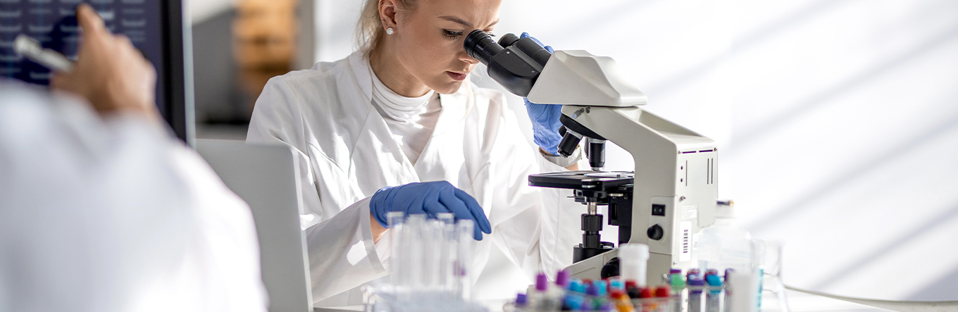 Frau in Labor schaut durch Mikroskop
