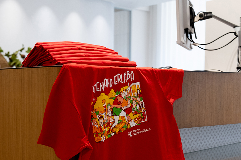 GLKB ESAF 2025 T-Shirt mit Themenbild «Mitenand erläbä» am Schalter in der Filiale in Glarus