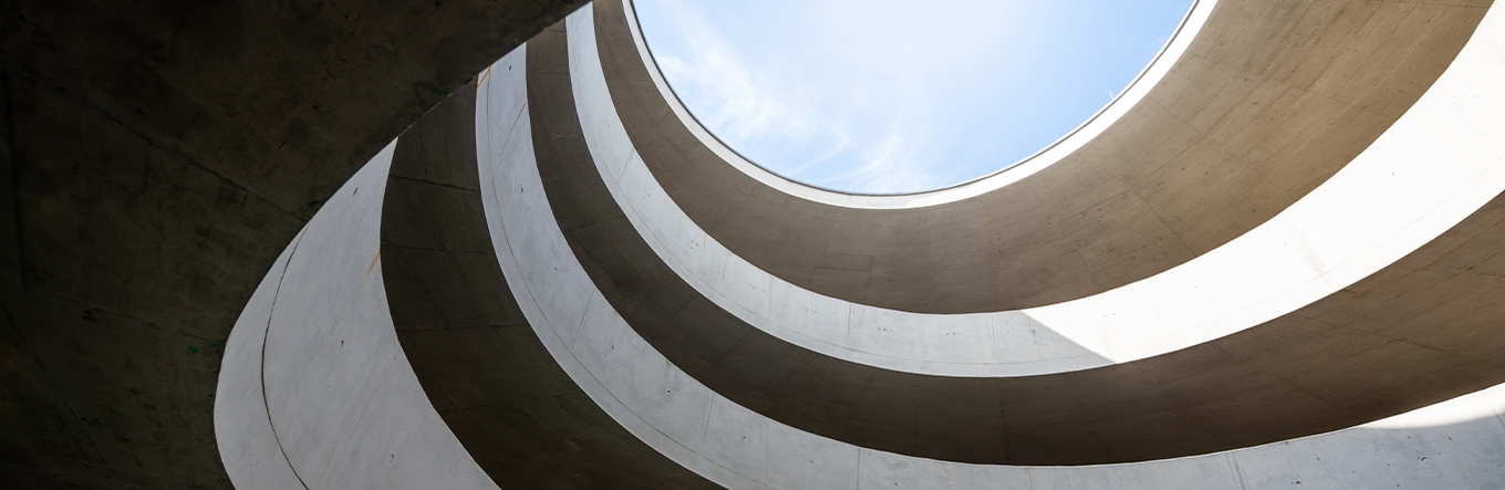 Abstrakte Architektur-Aufnahme vom inneren eines runden Gebäudes mit mehreren Stockwerken mit Blick nach oben auf den freien und blauen Himmel.