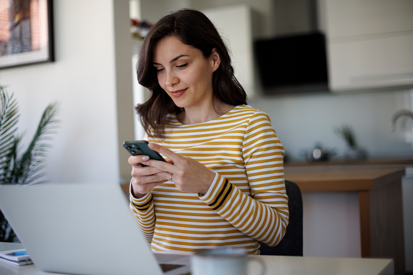 Frau mit Smartphone vor ihrem Notebook